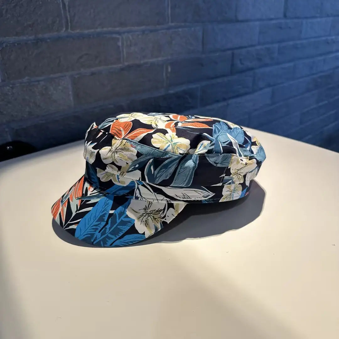 Gorra tipo bucket hat floral negra elegante, estilo coreano, impresa, con un patrón tropical vibrante en tonos azul, naranja y blanco.