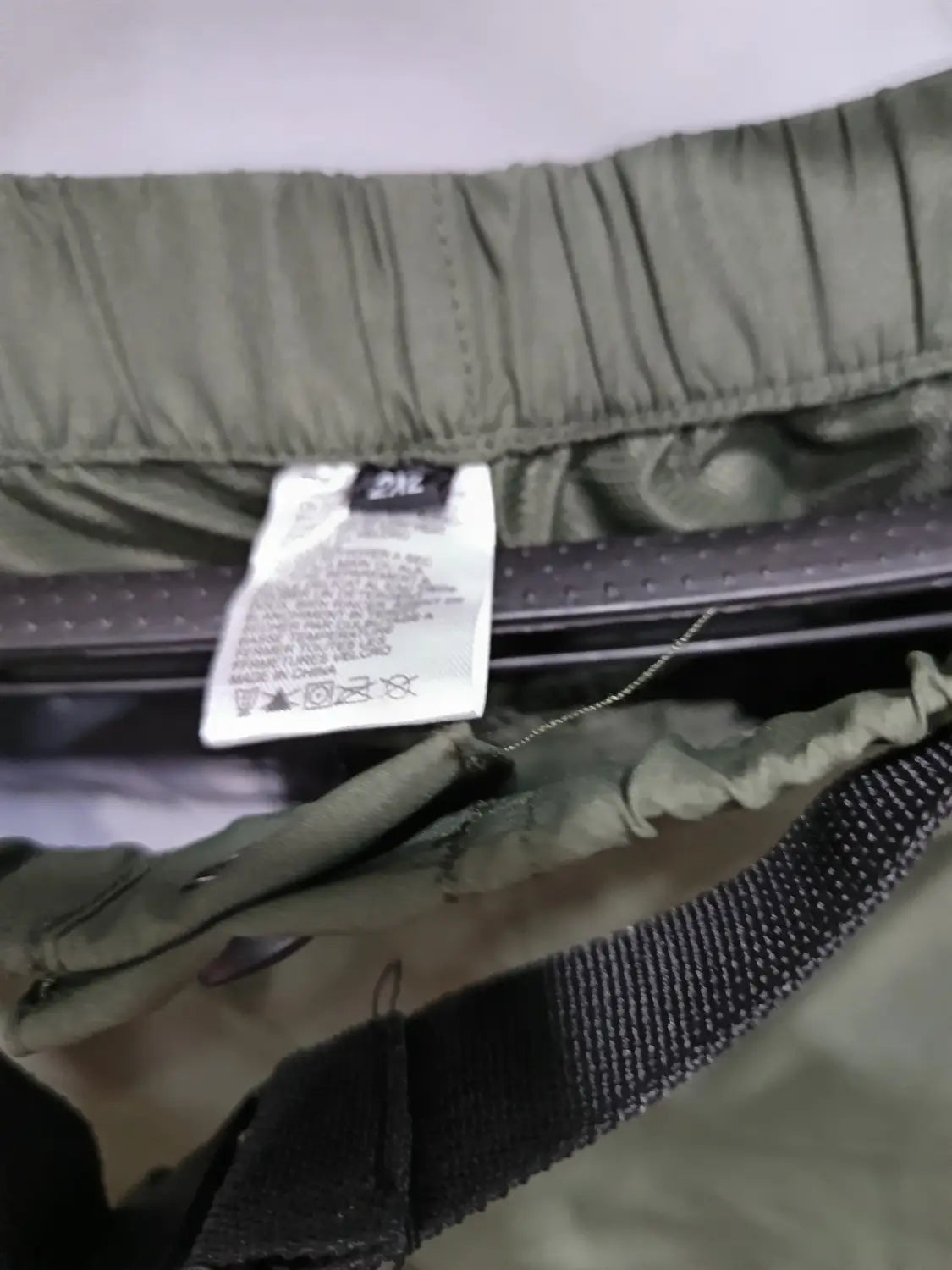 Convertible tactical hiking pants shown as olive green elastic-waist shorts with a black woven belt strap and a white care label attached to the inner waistband.