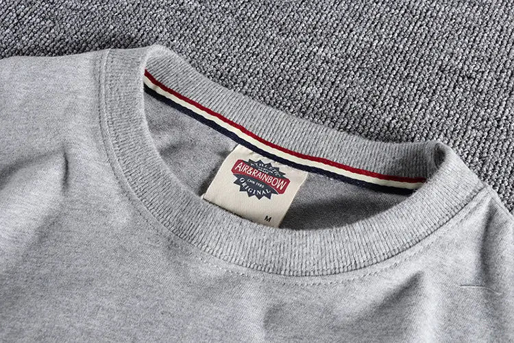 Camiseta de algodón jaspeado gris de color liso lavado de manga larga con etiqueta blanca con arcoíris y ribete a rayas en rojo, azul y negro a lo largo del cuello.
