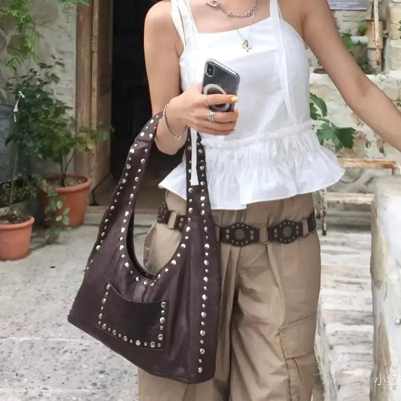 Brown studded leather shoulder bag with silver-toned metal studs and a front pocket designed as a retro hobo purse.