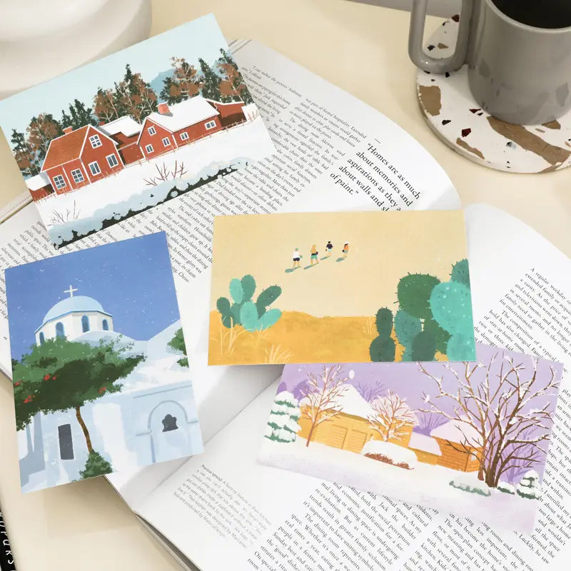 Four illustrated winter postcards from the Travel Diary Winter Postcards 15 pack featuring a church with snow-covered trees and desert cacti under a yellow sky for wall decor.