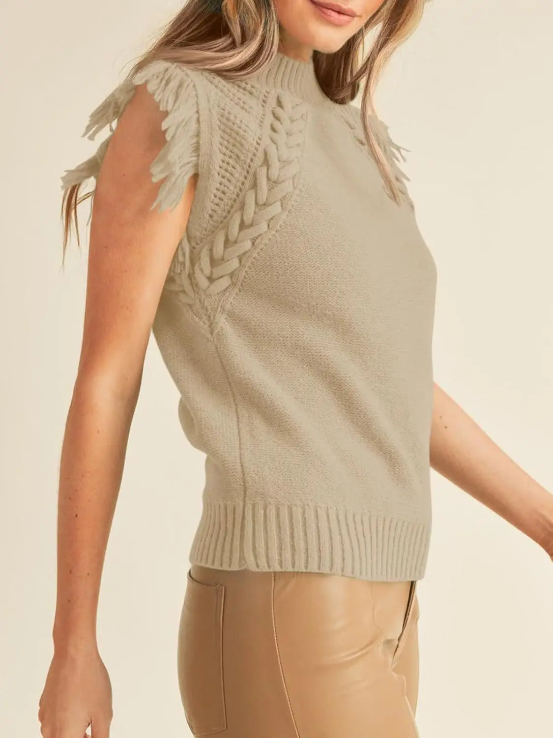 A taupe hand-woven fringed sleeveless knit sweater vest with a high neck, ribbed hem and cuffs, decorative braided panels on the shoulders, and fringed armhole detailing.