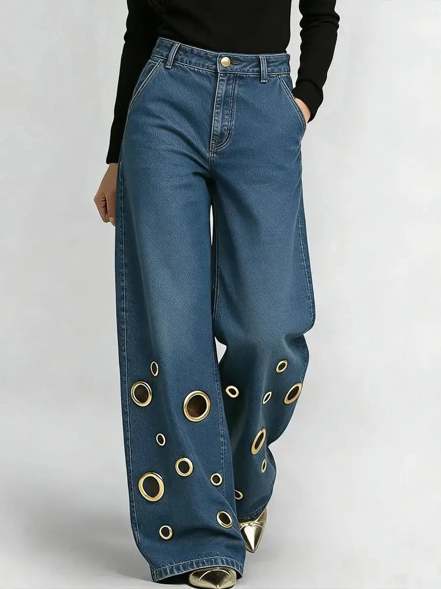 Jeans en denim bleu à jambes larges avec un motif audacieux d’œillets circulaires ton sur ton or le long des bas de jambes.