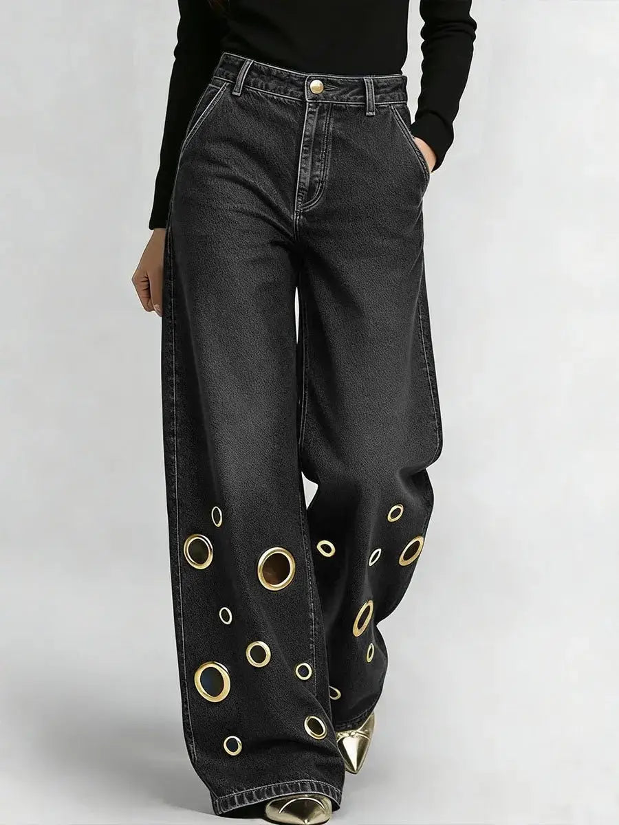 Jeans en denim noir à jambes larges présentant un motif asymétrique audacieux d’œillets circulaires ton sur ton or le long des bas de jambes
