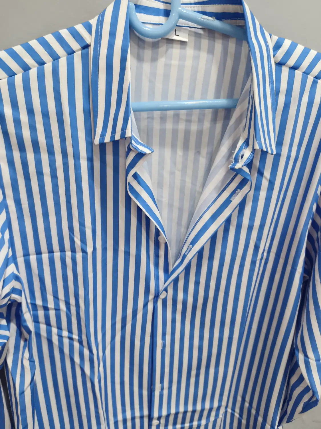Chemise décontractée à manches longues rayée verticalement bleu et blanc pour hommes, suspendue sur un cintre bleu clair.