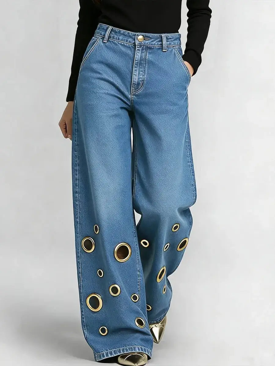 Jeans en denim bleu à jambes larges présentant un motif tendance d’œillets circulaires ton sur ton or le long des bas de jambes.