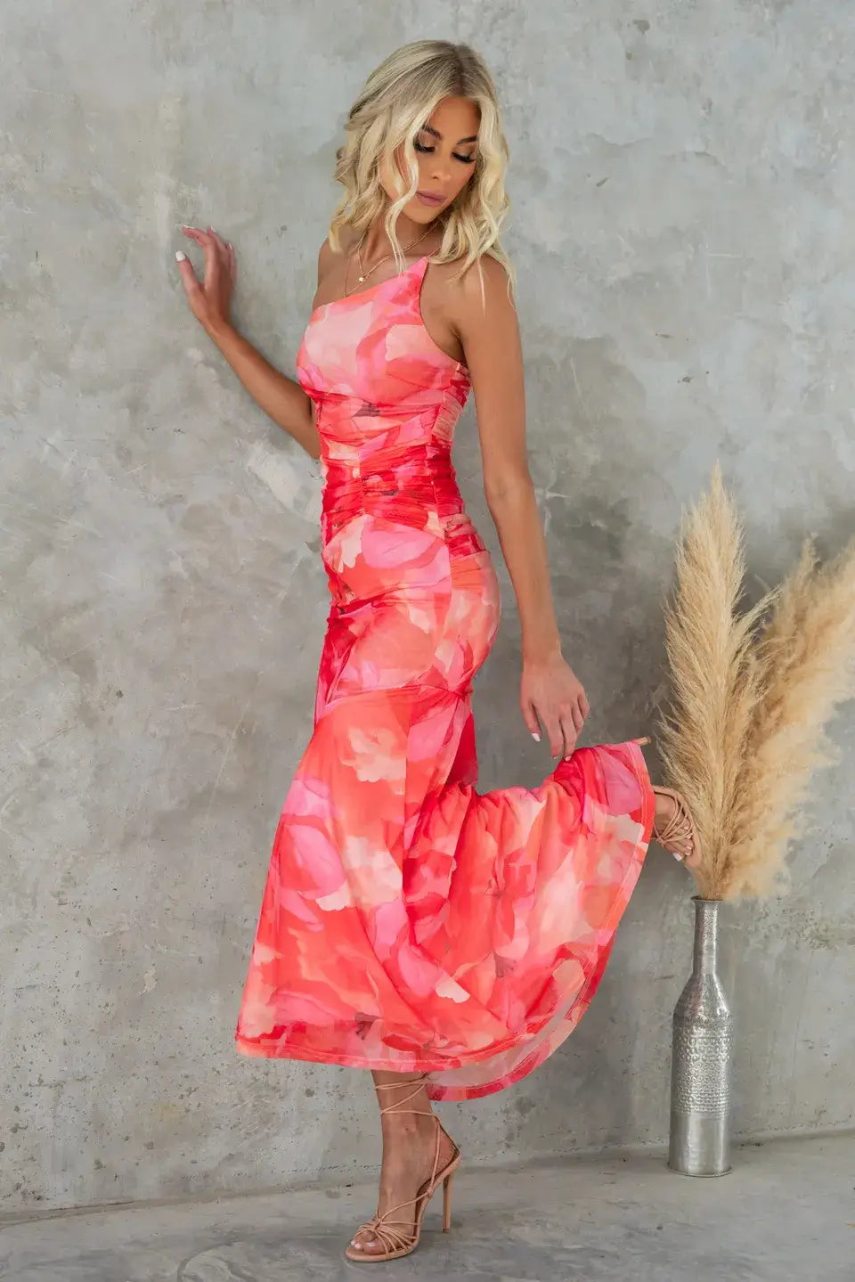 Une robe midi à imprimé floral corail et rose éclatant, avec une coupe une épaule réalisée dans un tissu fluide.