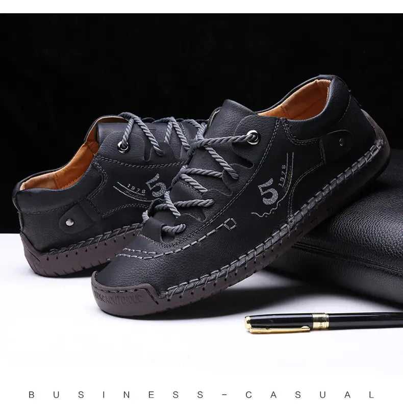 Herren-Lederschuhe im britischen Casual-Stil mit Schnürung in Schwarz mit grauen Schnürsenkeln, gestickten Zierdetails und einem Emblem „5 1978“ an der Seite.