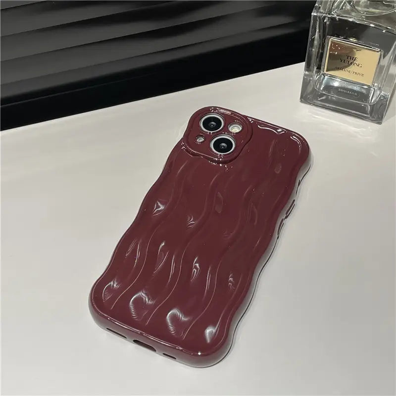 A glossy burgundy wavy liquid silicone iPhone case showing the back side with a textured surface.