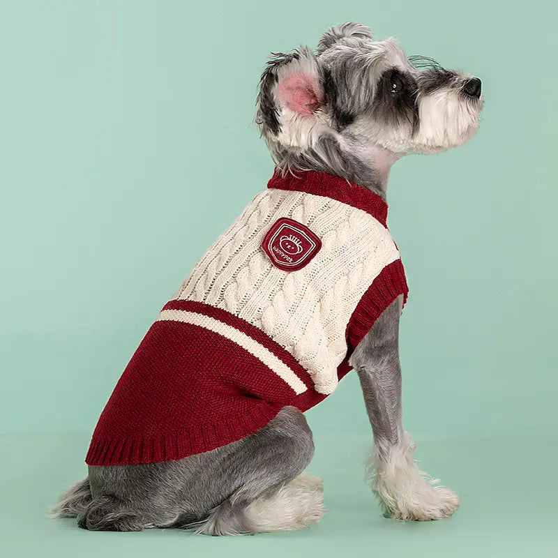 Ein gemütlicher cremefarbener und bordeauxroter Zopfmuster-Hundepullover mit rotem Aufnäher auf der Brust, entworfen als warme Schuluniform-Tierbekleidung.