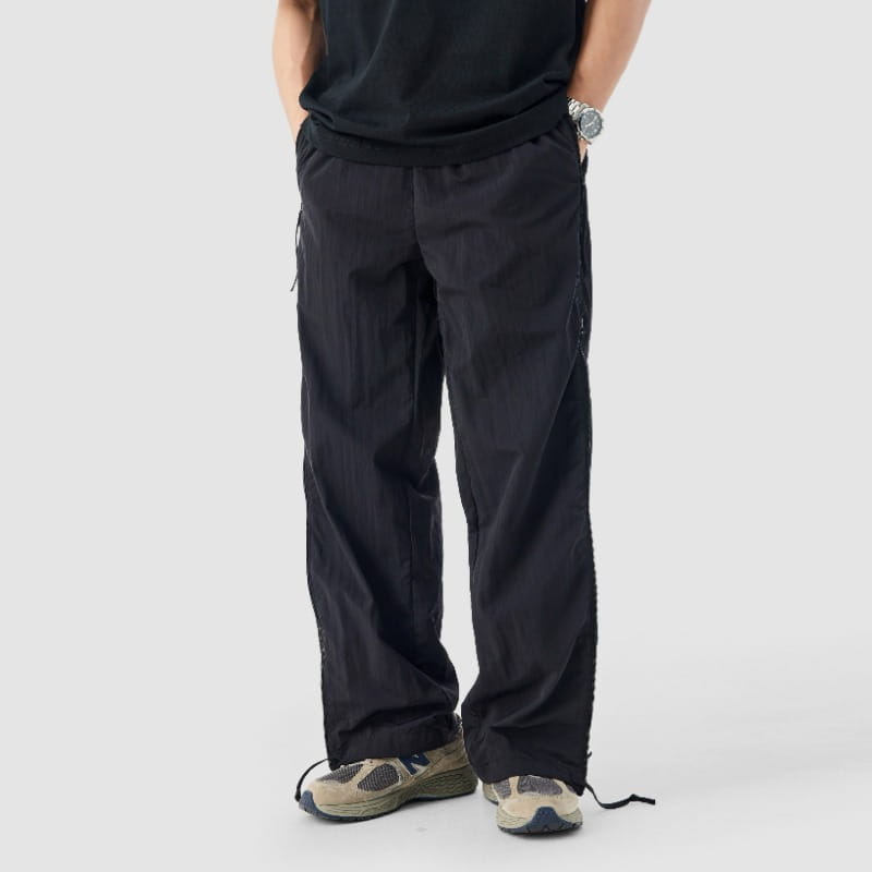 Pantalon de randonnée utilitaire noir à panneau latéral en mesh, présentant une conception cargo à jambe large, avec des poches latérales et des cordons de serrage aux chevilles.