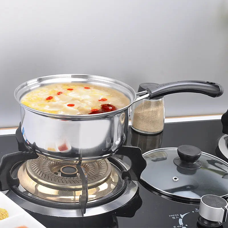 Olla de acero inoxidable brillante con asa negra de un juego de utensilios de cocina de acero inoxidable para inducción con tapas de vidrio, llena de sopa a fuego lento, decorada con bayas de goji rojas.