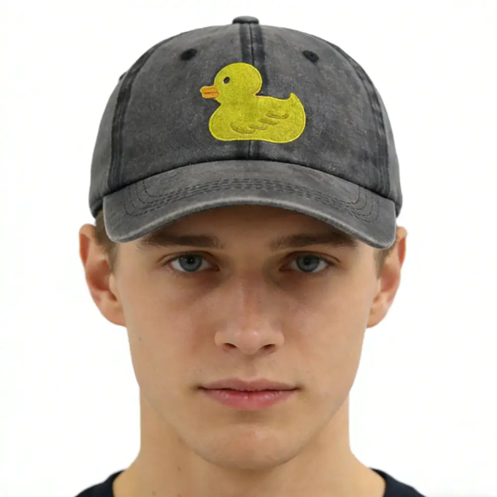 A faded gray distressed denim baseball cap featuring a bright yellow embroidered duck on the front.