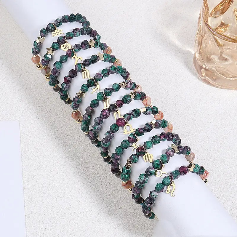 A set of natural stone zodiac constellation beaded bracelets featuring faceted green purple and pink gemstone beads with gold-toned metal charms.