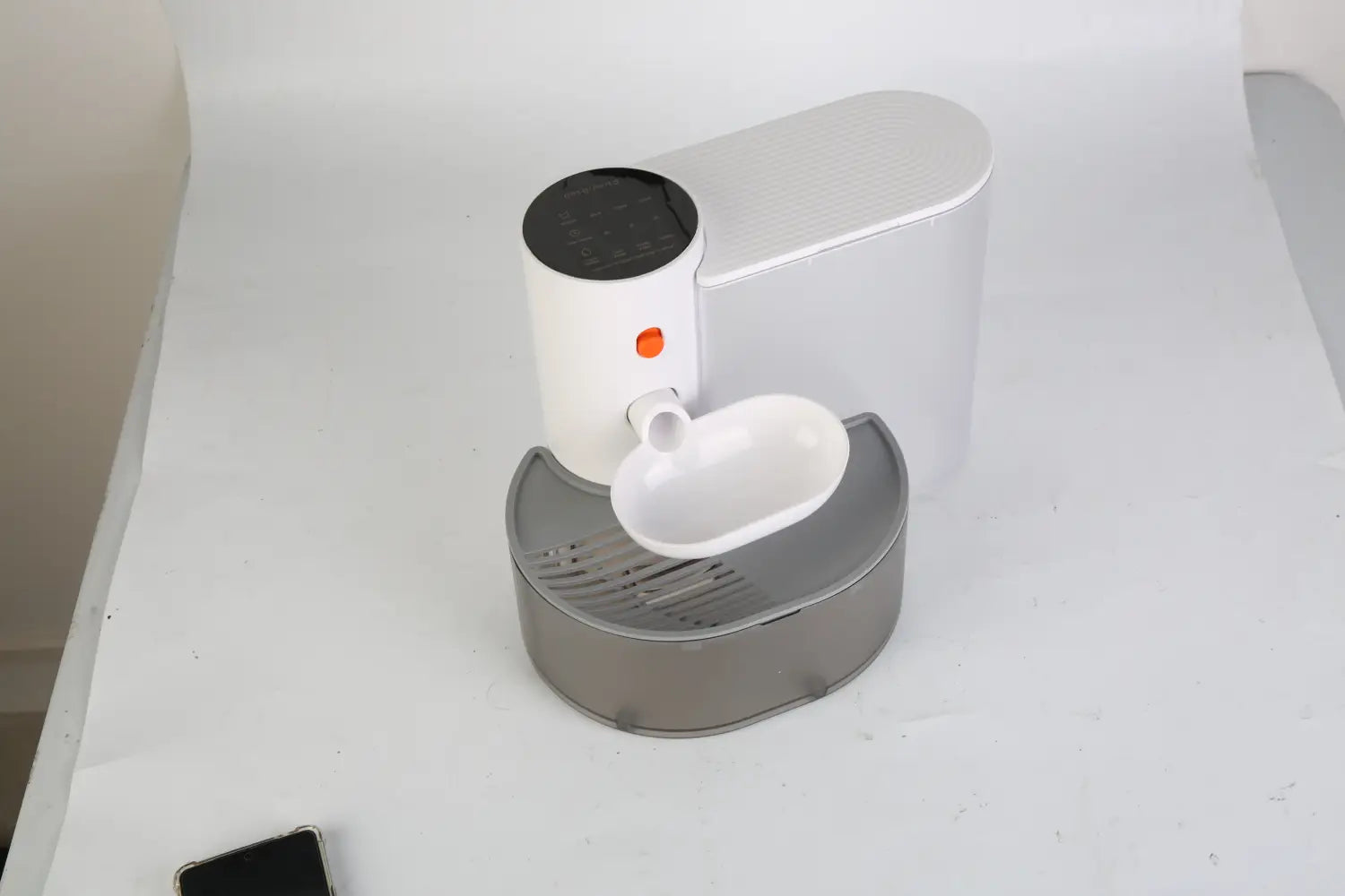 Distributeur automatique d’aliments pour animal de compagnie blanc et gris avec un dessus noir, un voyant indicateur orange et un plateau incurvé pour le déversement des aliments, présenté comme faisant partie du produit « fontaine à eau intelligente pour animal de compagnie de 3 L, sans fil, rechargeable, avec cuvette ».