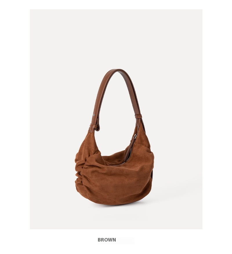 A soft brown suede dumpling shoulder bag with a single shoulder strap and subtle ruching details designed as a slouchy crossbody hobo.