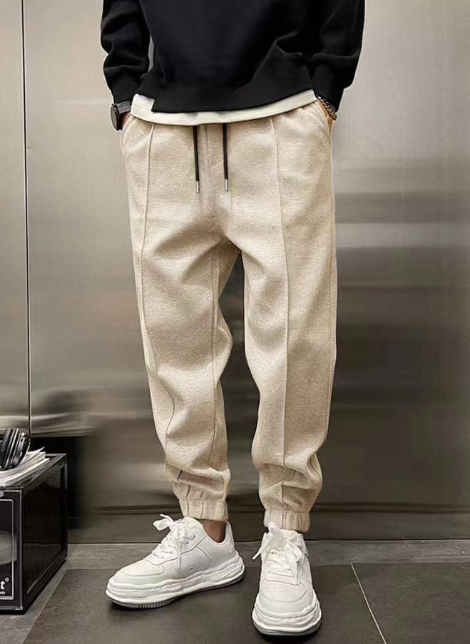Men’s fleece drawstring sweatpants in beige with black drawstrings, textured fabric, and elastic cuffs.