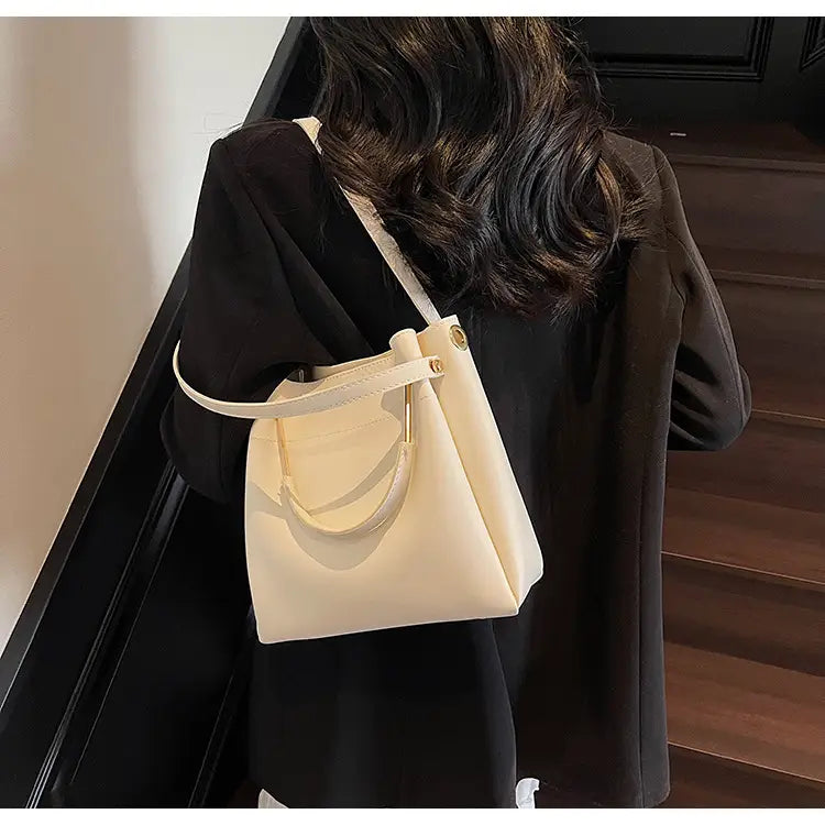 Cream-colored minimalist leather bucket bag with top handle and detachable adjustable shoulder strap.