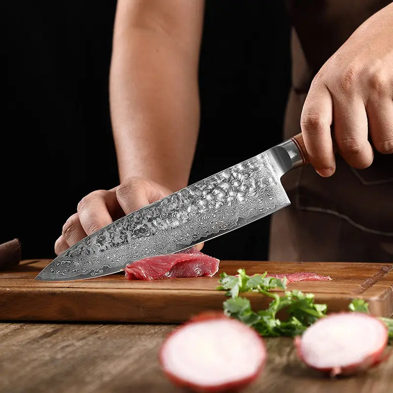 Un cuchillo de chef de acero damasco, elegante, con un patrón martillado y un mango de madera apoyado sobre una tabla de cortar junto a ingredientes frescos, como parte de un set de cuchillos de chef de 7 piezas con mango de madera martillado.