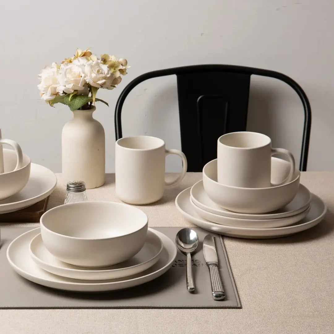 Juego de vajilla de gres de cerámica en tono marfil minimalista con acabado mate y líneas modernas y limpias; incluye 12 piezas con tazas diseñadas para su uso por tres personas.