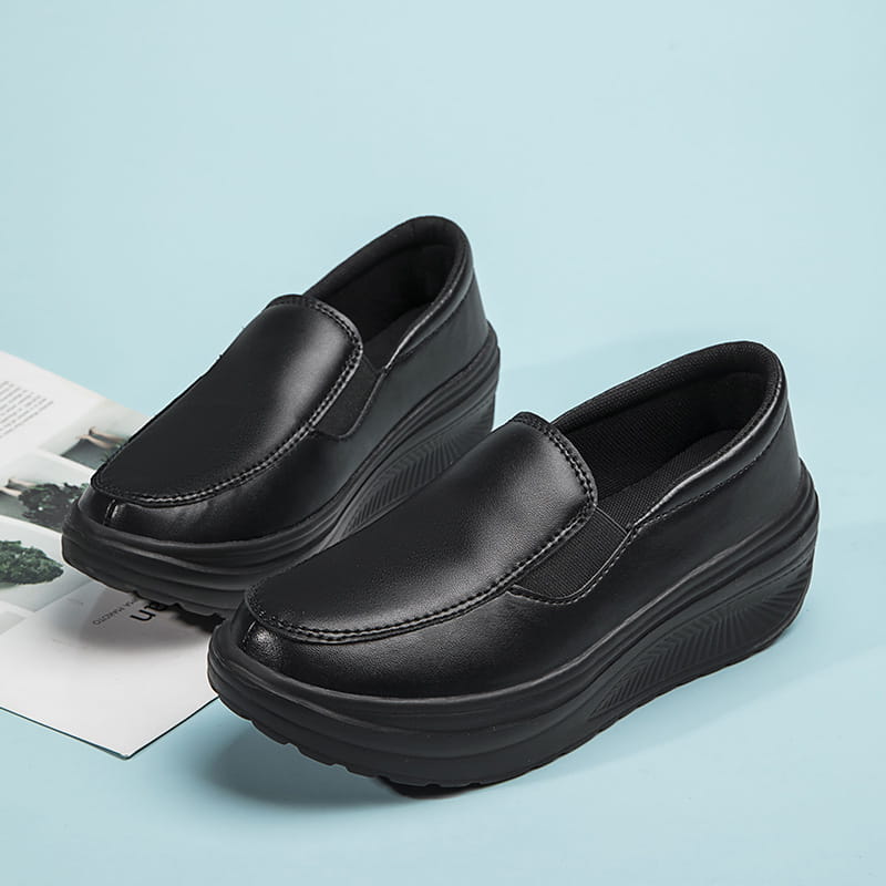 Chaussures slip-on à talon compensé en forme de coin en cuir noir, avec une semelle épaisse rembourrée, présentées depuis l’arrière.