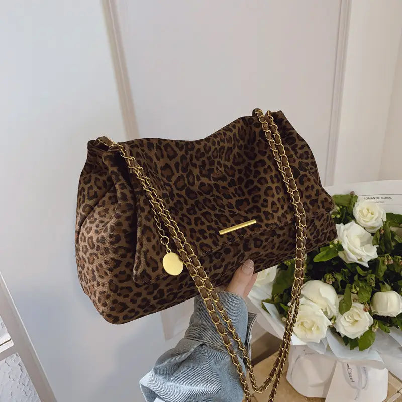 Brown leopard-print suede crossbody bag with gold-tone chain strap and circular pendant detail.