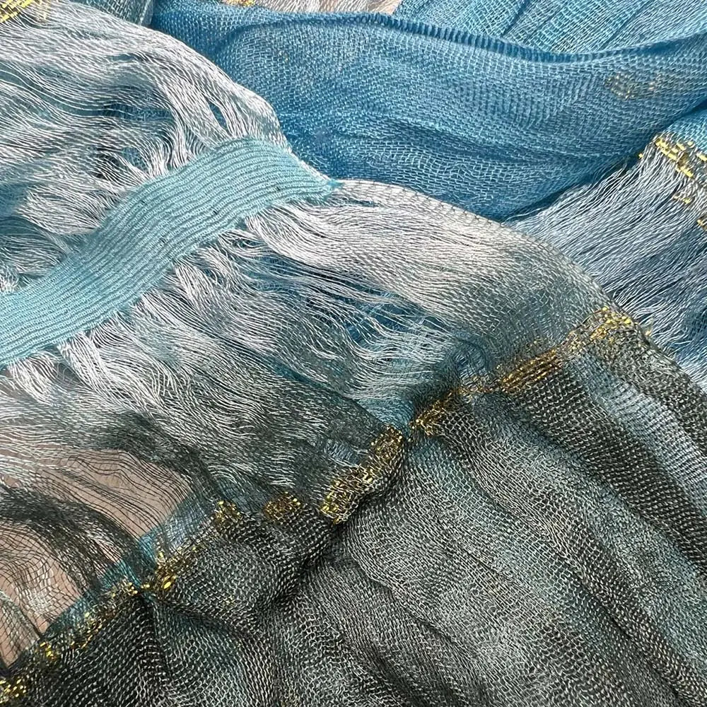 Una delicada bufanda entallada metálica turquesa confeccionada en malla translúcida azul y plateada con un ribete dorado brillante a lo largo de los bordes.