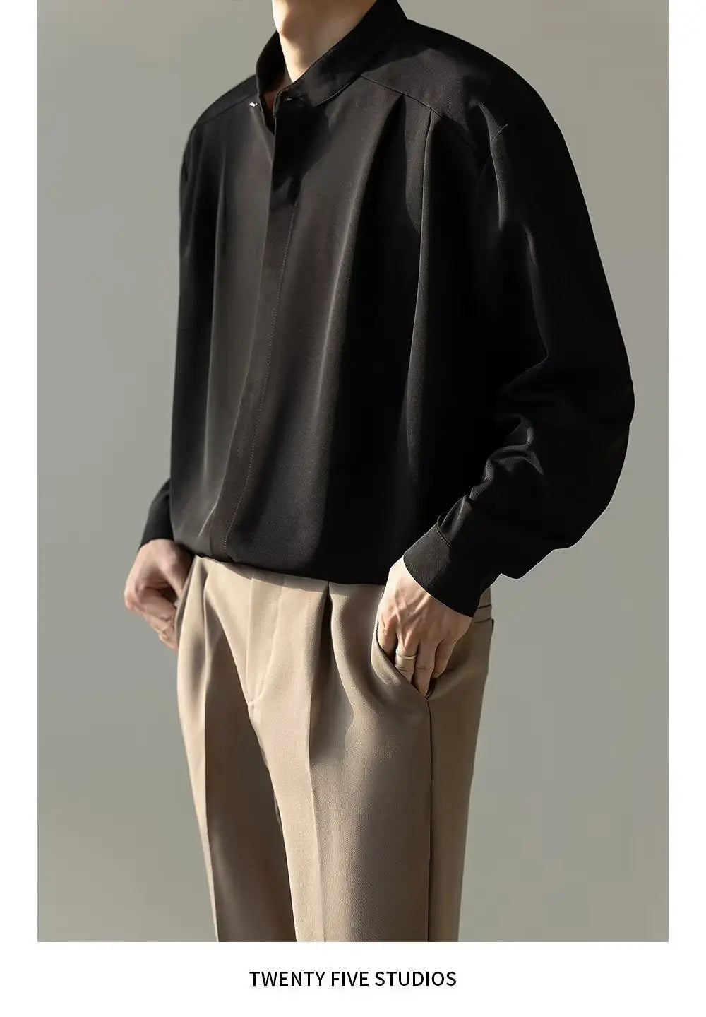 Chemise plissée pour homme à col montant en tissu type satin noir, avec manches longues, ouverture boutonnée sur le devant, brillance discrète et col structuré.