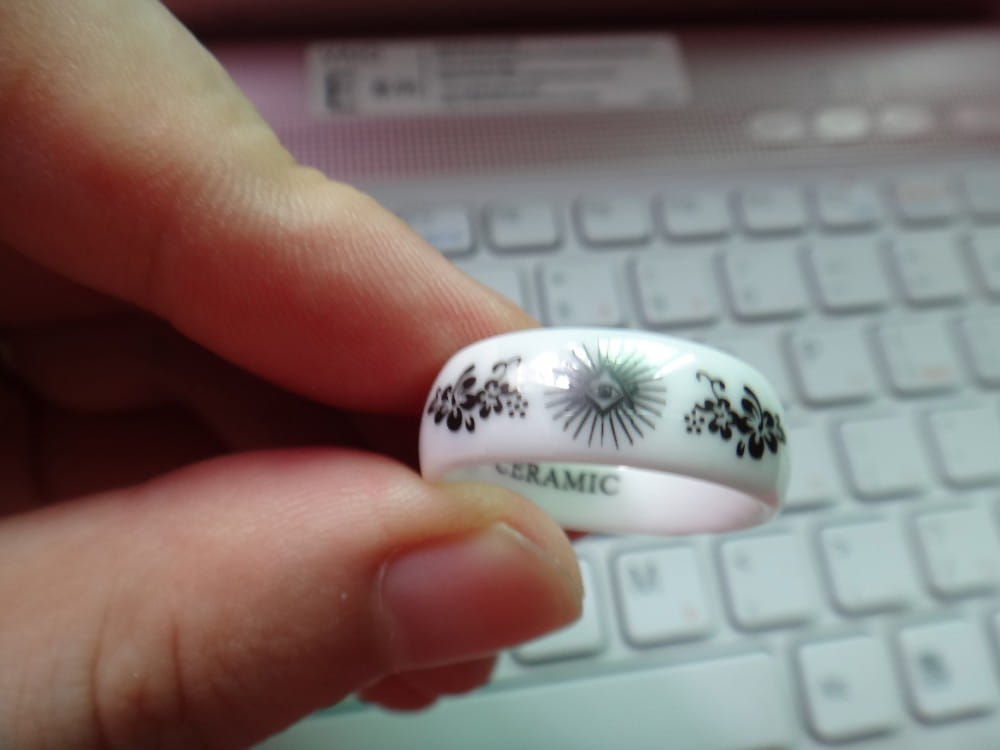 White ceramic ring with black floral and sunburst designs displayed alongside a black tungsten wedding ring with green aluminum 8mm band.