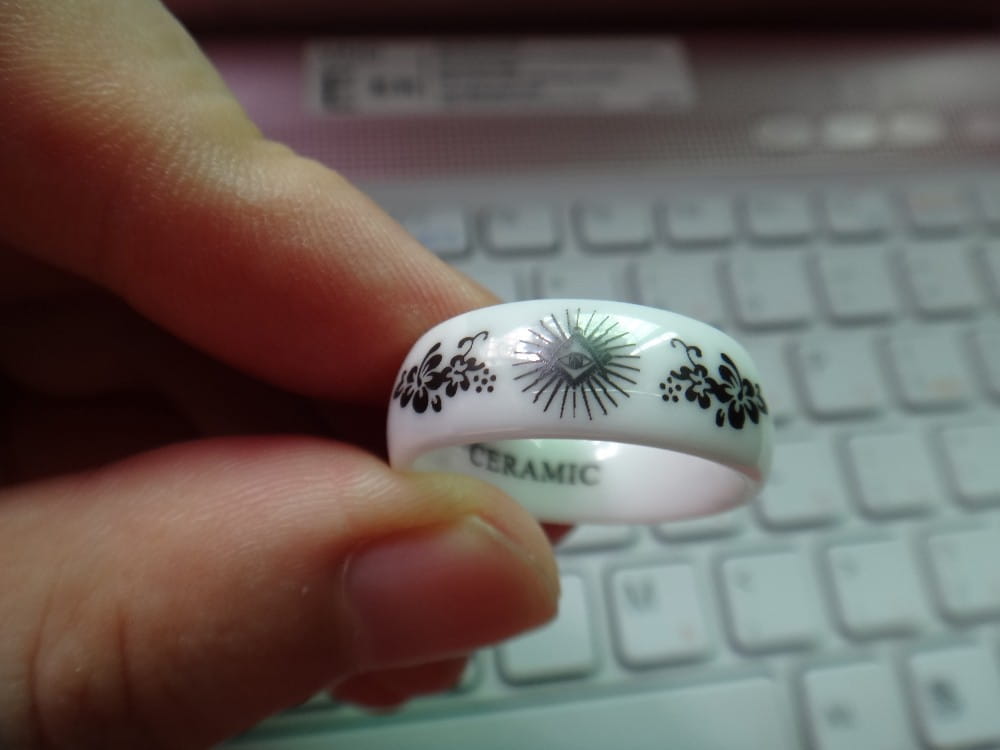 white ceramic ring with black floral and sunburst designs showcased alongside a black tungsten wedding ring with green aluminum 8mm band
