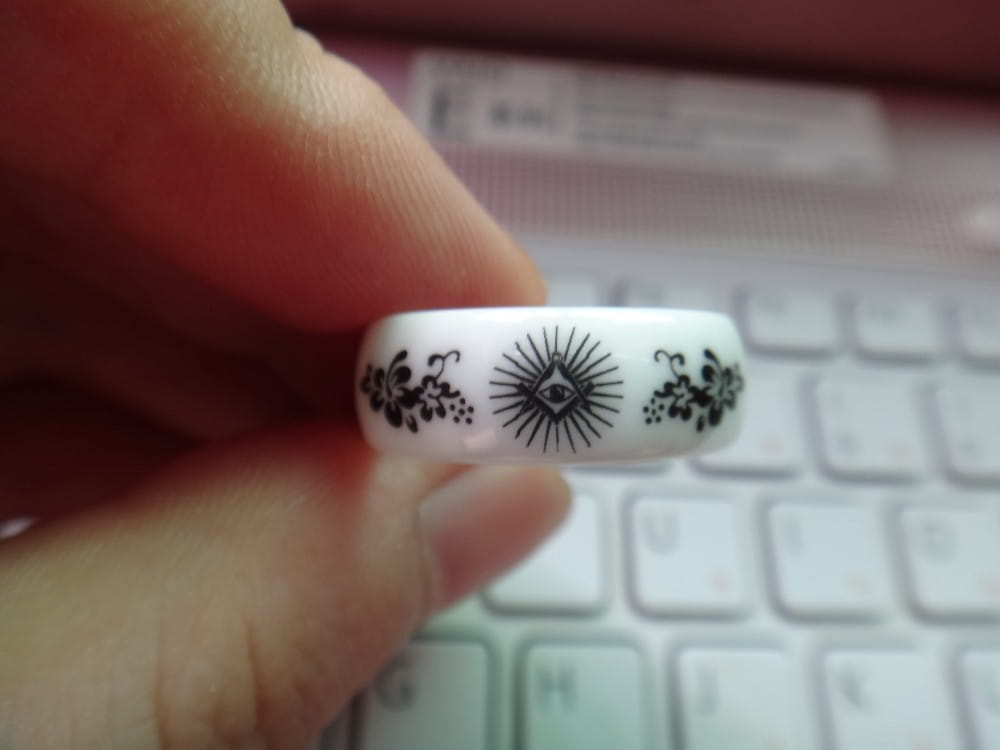 White ceramic ring with black floral and eye-of-panther designs complementing a black tungsten wedding ring with green aluminum 8mm band.