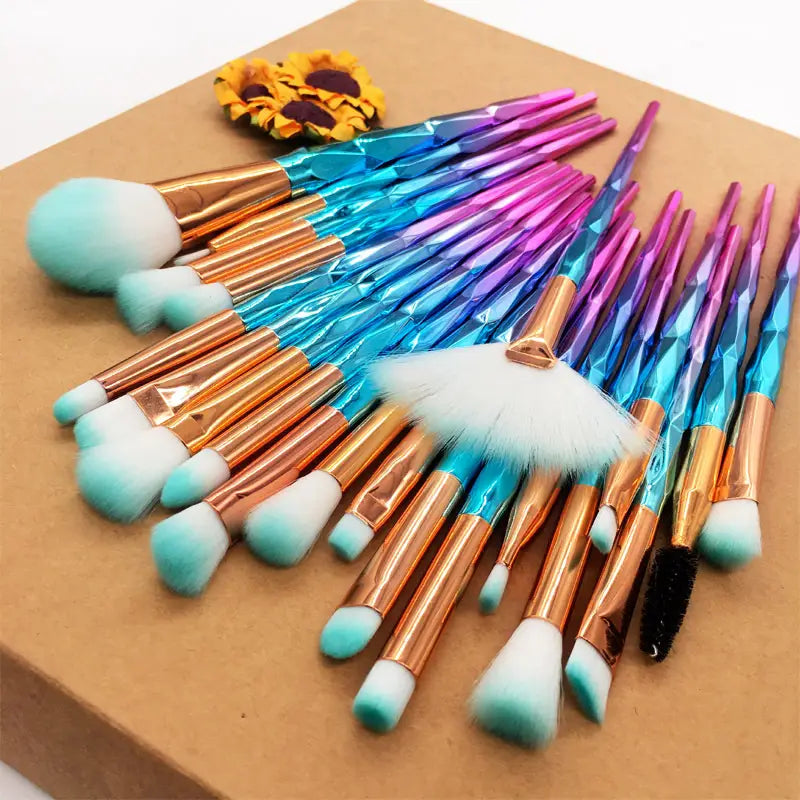 a set of 20 colorful makeup brushes with iridescent blue and purple faceted handles, rose gold ferrules, and soft teal tipped bristles from the makeup brush set 20 piece rose gold and glitter collection