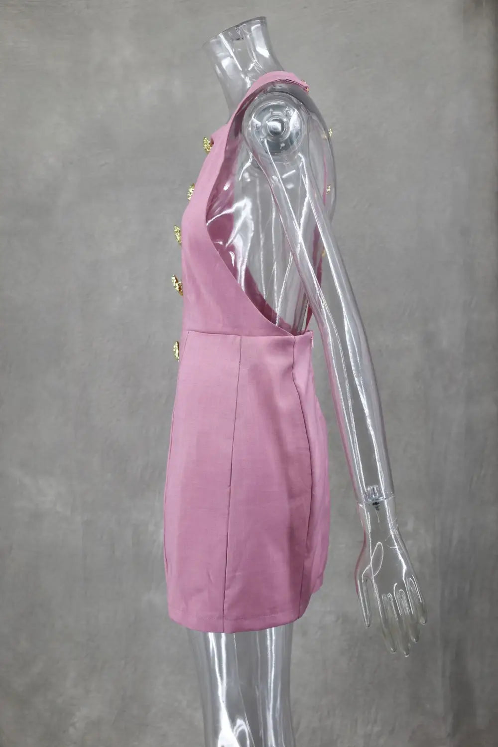 Une robe mini rose sans manches et dos nu, au style épuré, avec une coupe près du corps et des boutons décoratifs en forme de rose dorée dans le dos