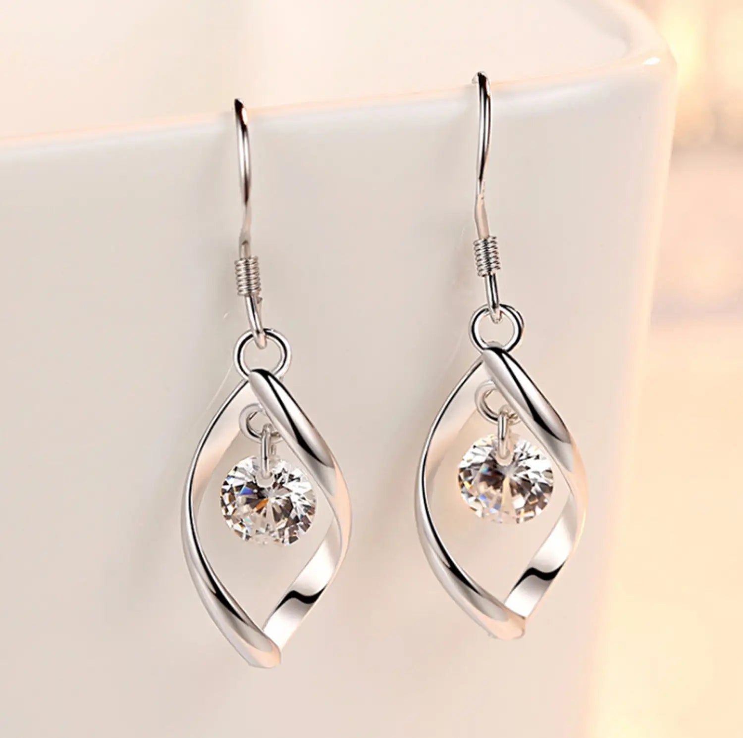 Twisted teardrop silver earrings featuring silver twisted wire design with a clear faceted crystal dangling at the center.