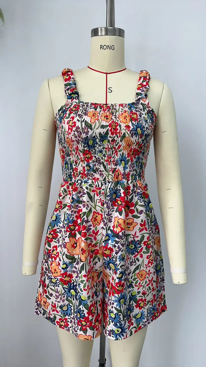 Mono tipo peto sin mangas de estampado floral vibrante con tirantes de hombro con frunces y cintura fruncida, presentado en un maniquí para vestir en la playa durante el verano.