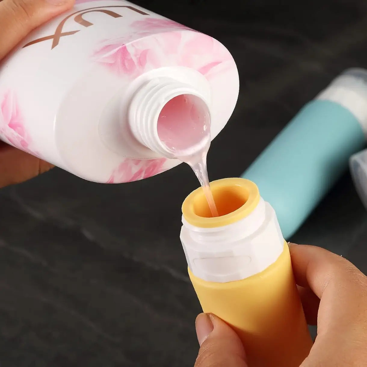 un flacon de voyage en silicone blanc réutilisable, avec un motif floral rose, versant un liquide dans un distributeur de voyage anti-fuite jaune et blanc, dans un ensemble de flacons de voyage en silicone réutilisables anti-fuite