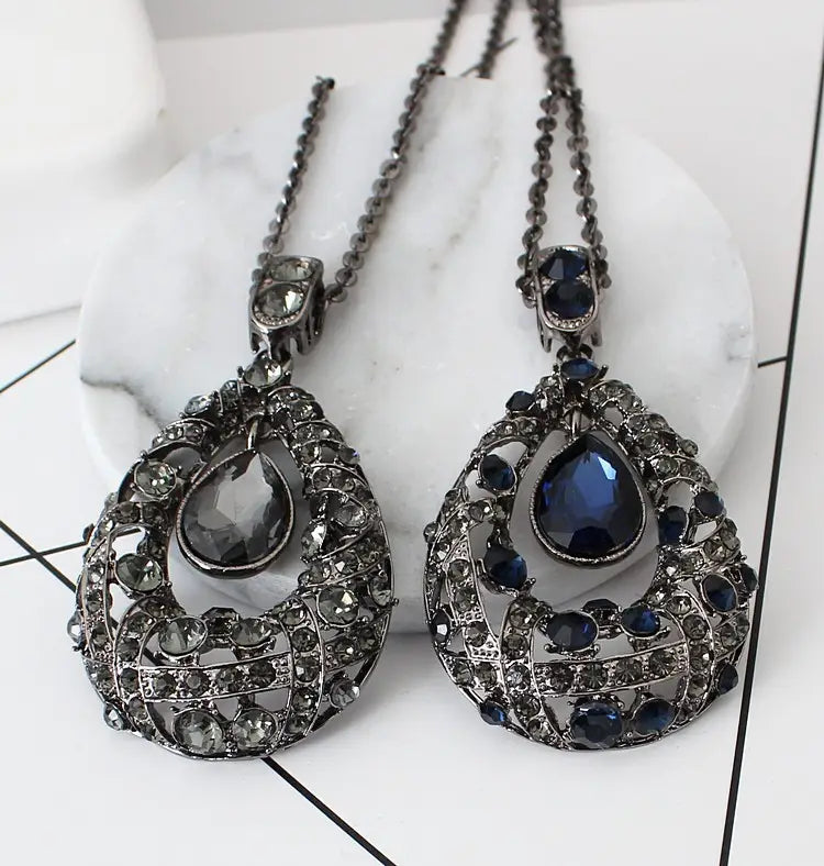 Elegant teardrop-shaped pendant necklace featuring intricate metalwork with sparkling black and deep blue crystals on a Korean style sweater chain.
