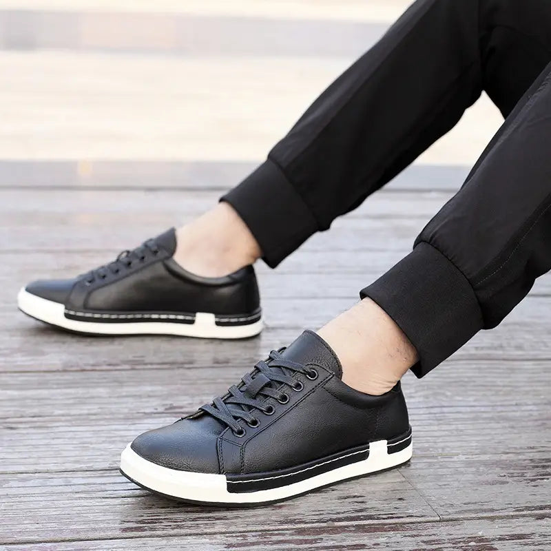 Les baskets basses en cuir pour homme, faites à la main, de couleur noire, avec des semelles en caoutchouc blanc et des coutures noires contrastantes, conçues pour un usage décontracté.
