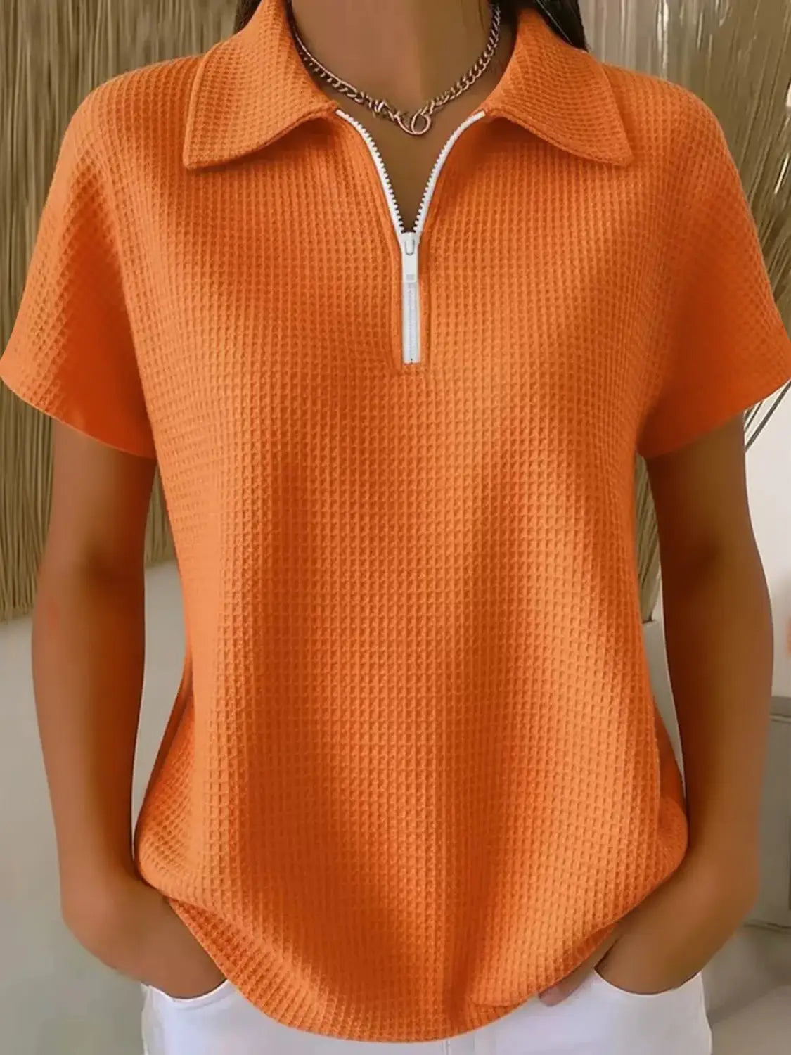 Vibrant orange waffle knit half zip short sleeve polo shirt featuring a white zipper and collar.