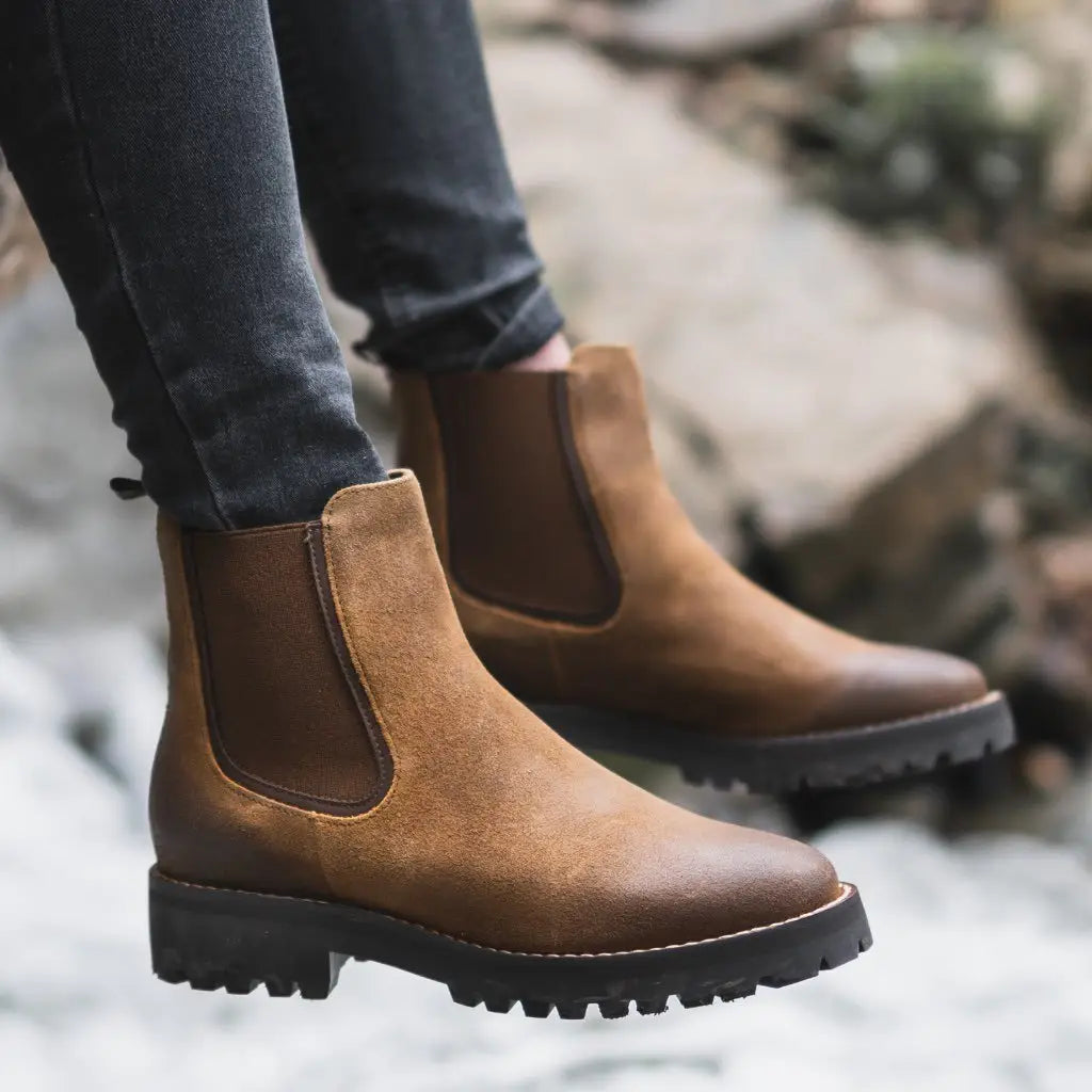 Brown suede Chelsea boots with a chunky black rubber platform sole shown from the back side.