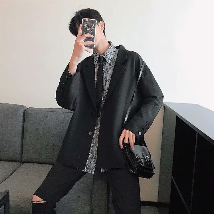 black leather satchel with silver toned hardware and a structured minimalist design shown with mens loose casual thin suit jacket.