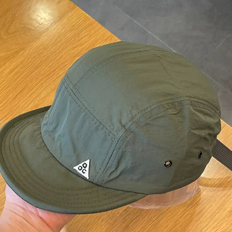 Olive green five-panel quick drying short brim cap with a white triangular logo on the front, designed for active wear.