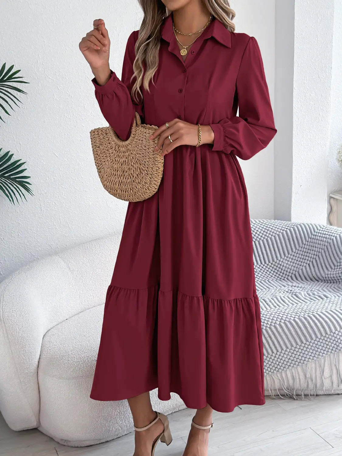 A woman wears a long-sleeved burgundy midi dress with tiered hem and button-down front featuring a collar.