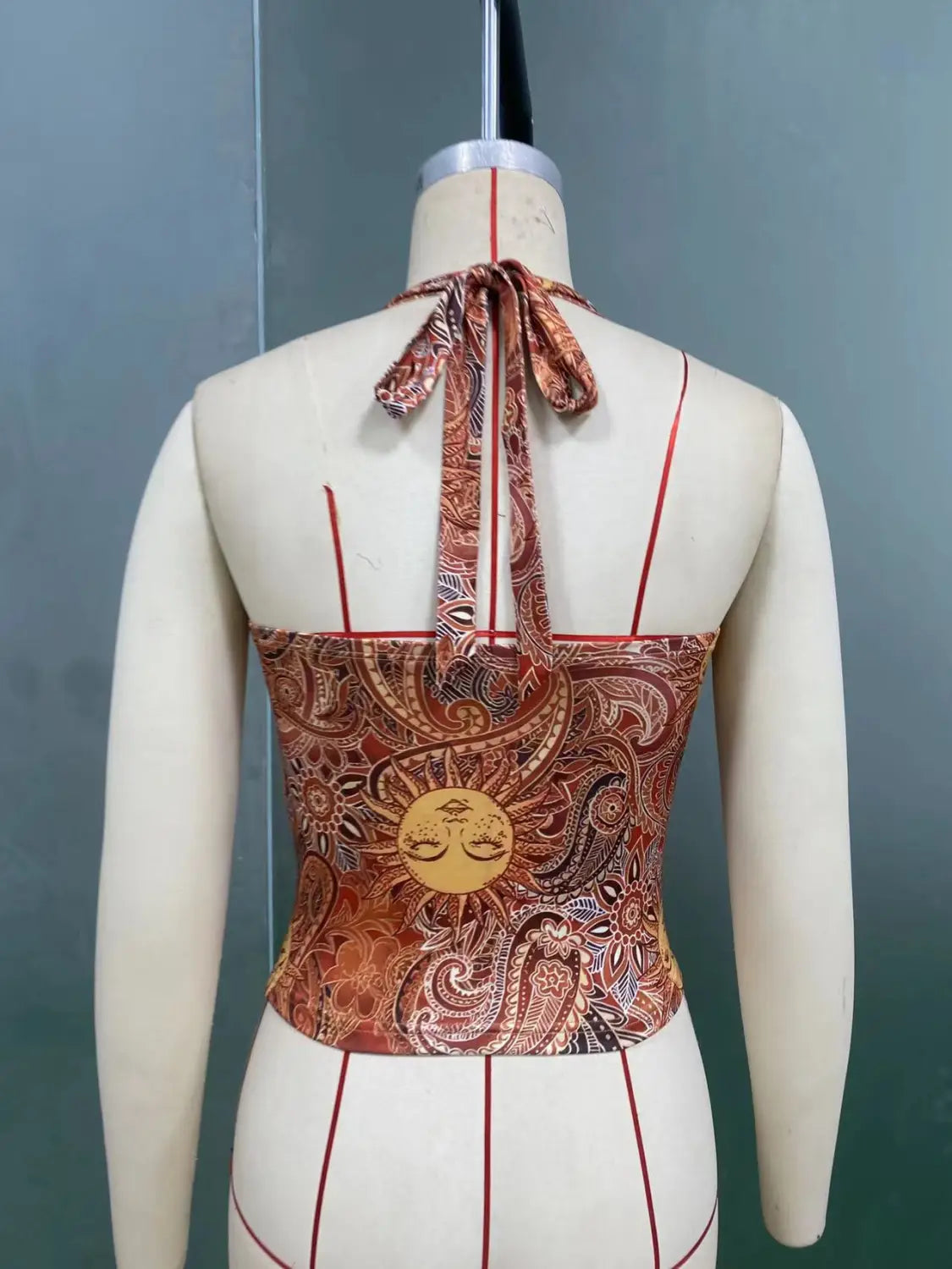 Ein eng anliegendes Paisley-Haltertop in Rost- und Brauntönen mit einem reichen, aufwendigen Muster und einem zentralen goldenen Sonnenmotiv auf der Rückseite.