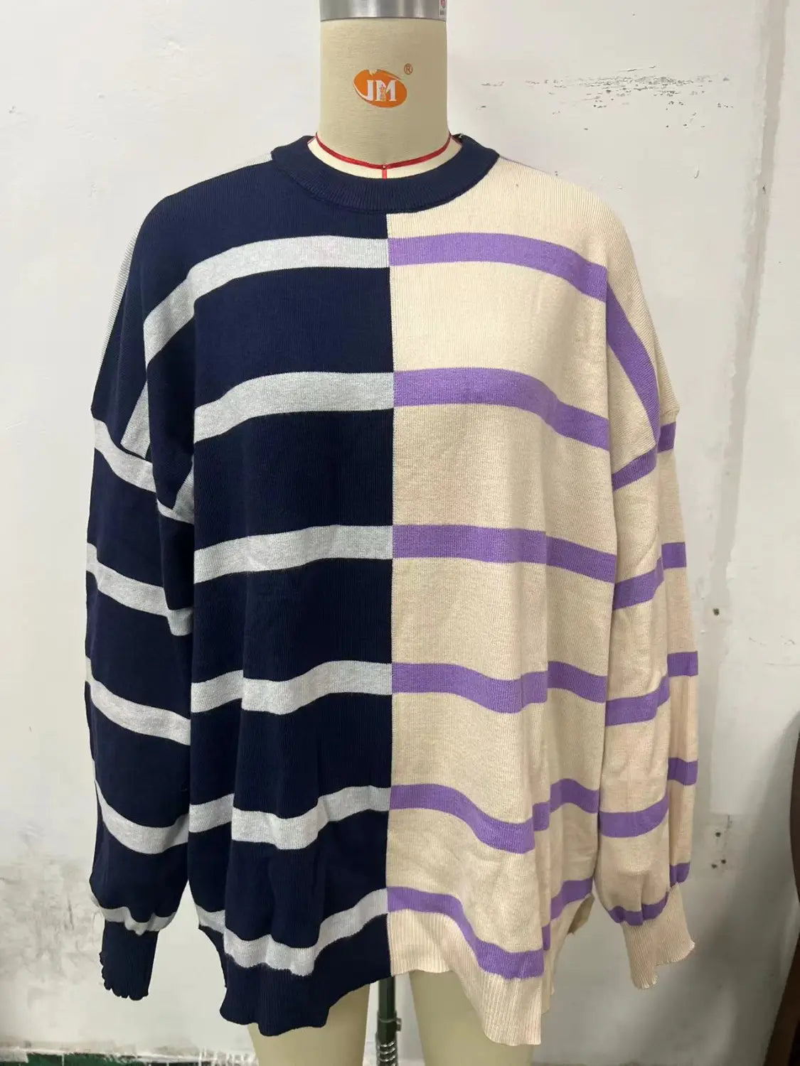 A cozy women’s oversized knit sweater featuring a bold two-tone split color striped design with navy blue and white stripes on one side and cream and purple stripes on the other.