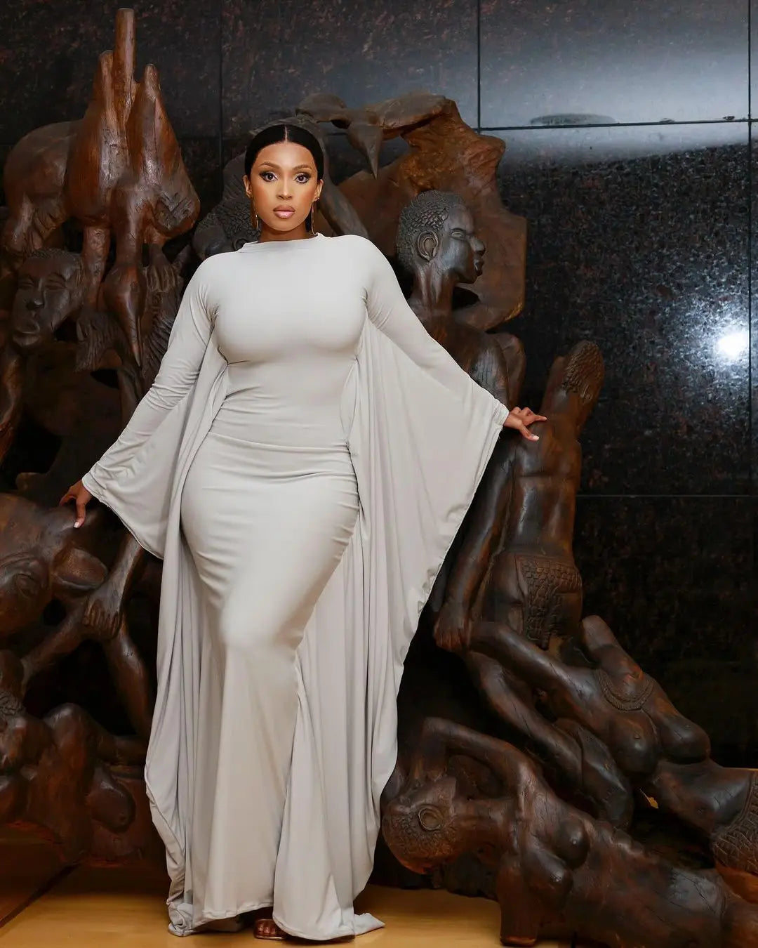 a flowing light gray satin maxi dress featuring asymmetrical batwing long bell sleeves and a high neckline.