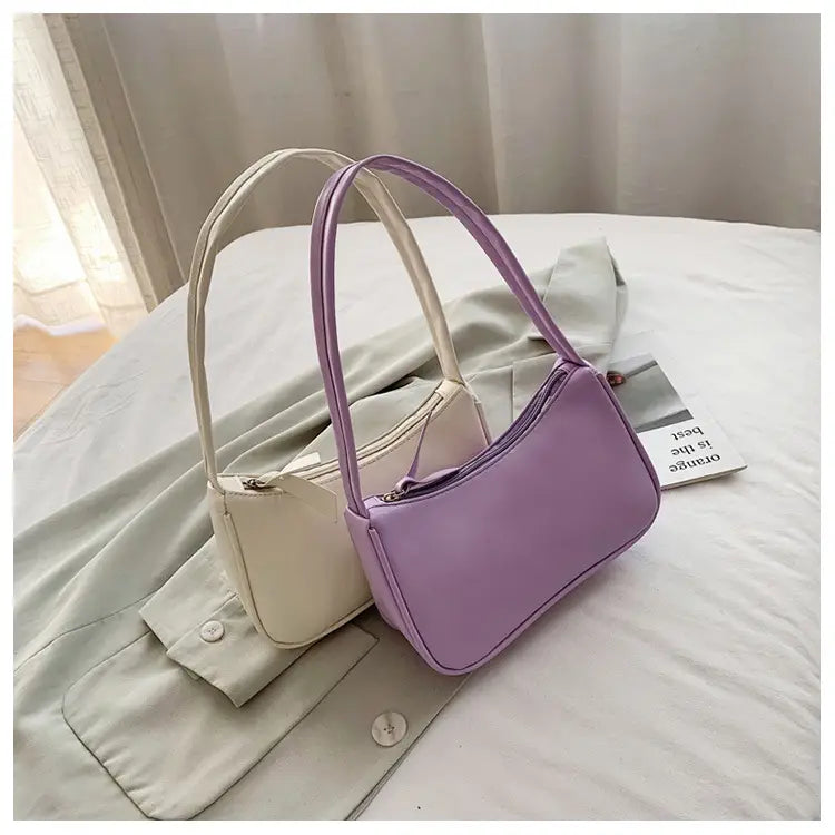 Eine elegante lavendelfarbene minimalistische Umhängetasche aus Kunstleder mit gebogenem Unterarmgriff, mit glatter glänzender Oberfläche und passendem Schulterriemen.