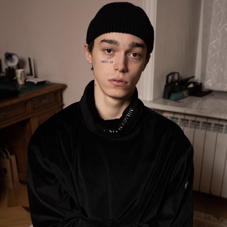 black velvet hoodie with a high collar and white lettering along the neckline paired with a dark gray ribbed wool beanie hat.