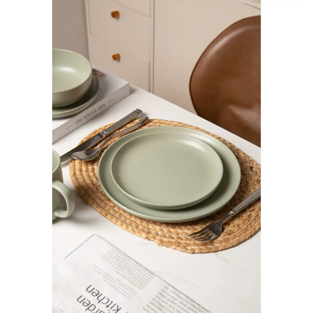 ensemble de vaisselle en céramique vert sauge à finition mate, assiettes empilées sur un dessous de table tissé, issu d’un ensemble de vaisselle en grès cérame de 12 pièces pour trois personnes