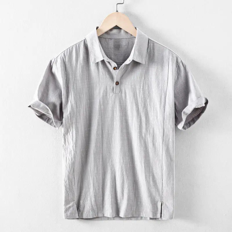 Chemise en lin pour homme gris clair à manches courtes, réalisée dans un tissu texturé de type lin, avec fermeture boutonnée en bois, conçue comme un haut d’été décontracté et respirant.